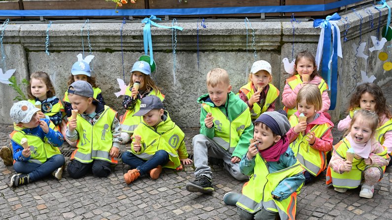 Auf dem Bild ist eine Kitagruppe vor dem Brunnen beim Eis essen zu sehen. 
