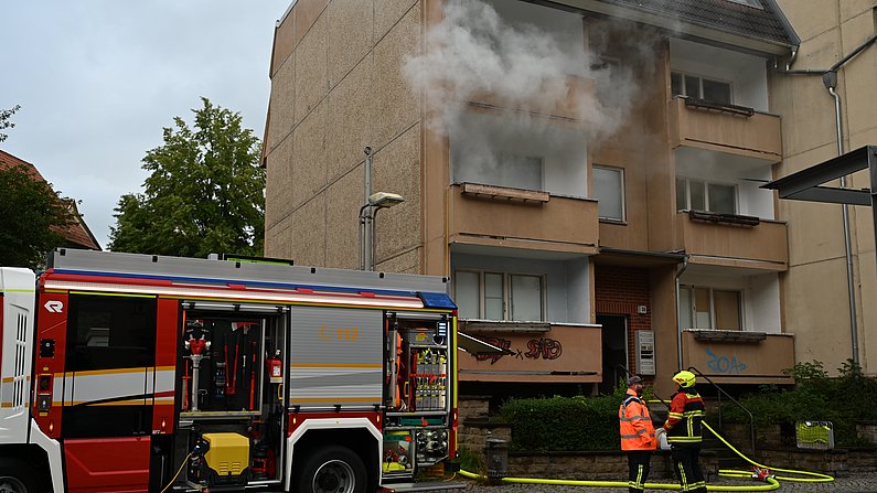 Auf dem Foto sieht man ein leerstehendes Gebäude. Aus eriner Wohung dringt Rauch nach außen. Vor dem Haus steht die Feuerwehr. 