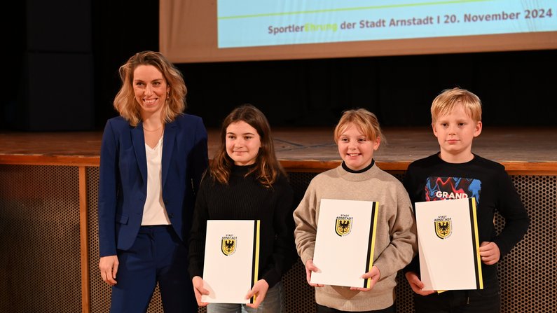 Auf dem Foto sind 3 Kinder und eine Frau zu sehen. Alle lächeln. Die Kinder halten eine Urkunde in den Händen. Auf dem Foto sind 3 Kinder und eine Frau zu sehen. Alle lächeln. Die Kinder halten eine Urkunde in den Händen.