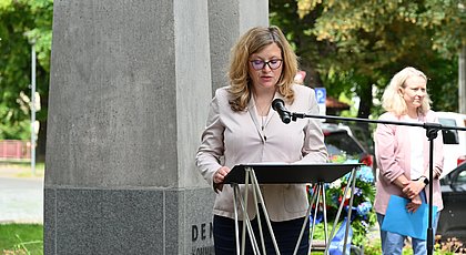 Auf dem Foto ist eine Frau zu sehen, sie hält eine Rede und spricht in ein Mikrofon. 