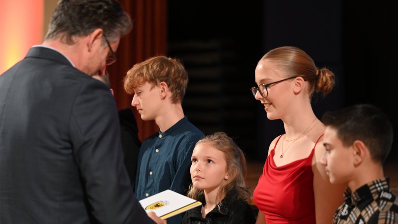 Auf dem Foto sind 5 Personen zu sehen. Ein Mann überreicht einem Kind eine Urkunde. Auf dem Foto sind 5 Personen zu sehen. Ein Mann überreicht einem Kind eine Urkunde.