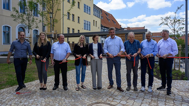 Auf dem Bild sind neun Personen beim Durchschnitt eines roten Bandes zu sehen. Auf dem Bild sind neun Personen beim Durchschnitt eines roten Bandes zu sehen.