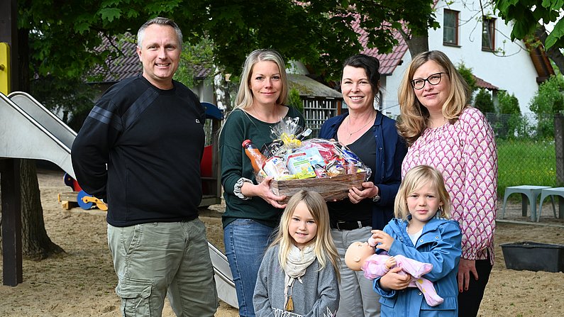 Auf dem Foto sind vier Erwachsene und zwei Kinder zu sehen. Eine Frau hält einen Präsentkorb vor sich. Alle lächeln. 