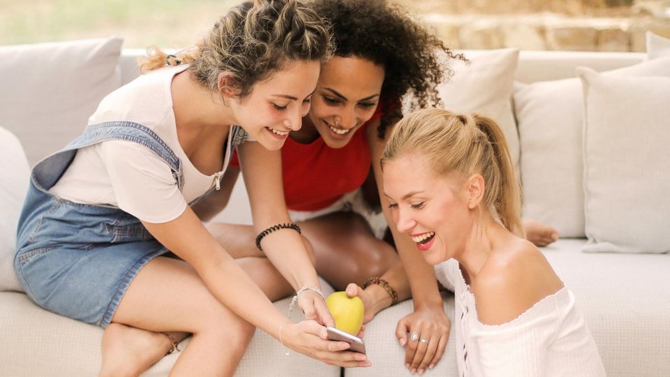 Das Bild zeigt drei Frauen, die den Newsletter auf einem Handy lesen