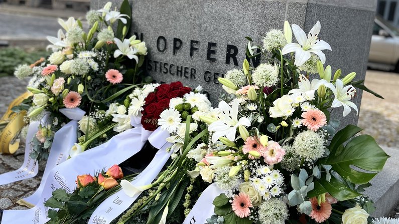 Auf dem Bild sind Blumengestecke an der Gedenkstele der „Opfer kommunistischer Gewalt 1945-1989“ zu sehen.