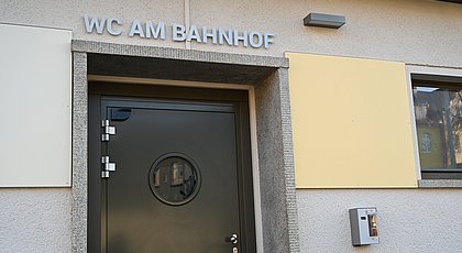 Auf dem Foto ist der Schriftzug: WC am Bahnhof zu sehen sowie die Eingangstür zur Toilettenanlage.