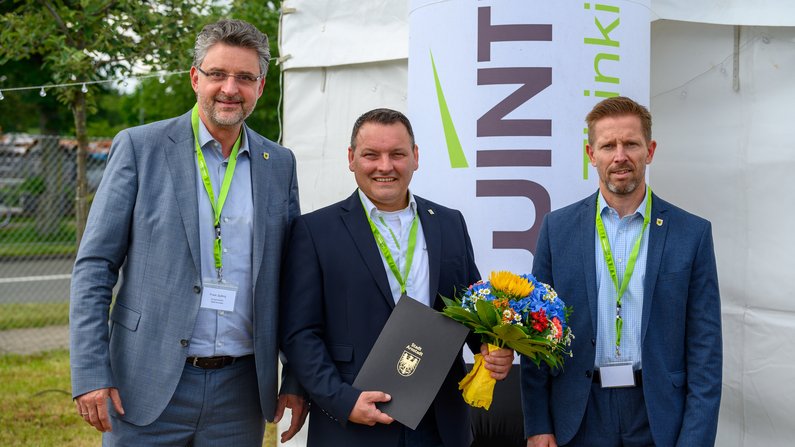 Drei Männder schauen freundlich in die Kamera. Sie stehen vor einem Festzelt. Der Mann in der Mitte hat einen Blumenstrauß und eine Urkunde in der Hand. Drei Männder schauen freundlich in die Kamera. Sie stehen vor einem Festzelt. Der Mann in der Mitte hat einen Blumenstrauß und eine Urkunde in der Hand.