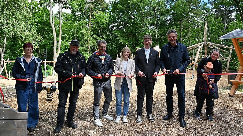 Auf dem Foto sind acht Personen zu sehen, die ein rotes Band durchschneiden. es wurde ein Spielplatz eingeweiht. Auf dem Foto sind acht Personen zu sehen, die ein rotes Band durchschneiden. es wurde ein Spielplatz eingeweiht.