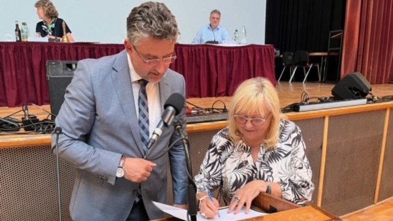 Ein Mann und eine Frau stehen am Pult. Sie unterschreibt einen Zettel. Ein Mann und eine Frau stehen am Pult. Sie unterschreibt einen Zettel.