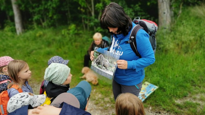 Auf dem Bild ist eine Frau von der NABU zu sehen, die Kindern Biberschäden erklärt. Auf dem Bild ist eine Frau von der NABU zu sehen, die Kindern Biberschäden erklärt.